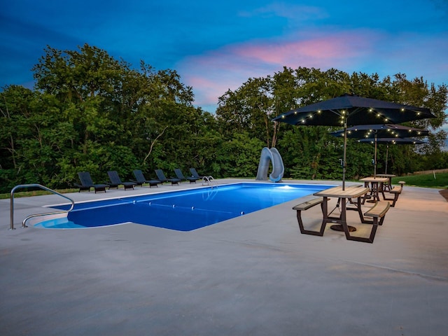 pool at dusk featuring a water slide and a patio