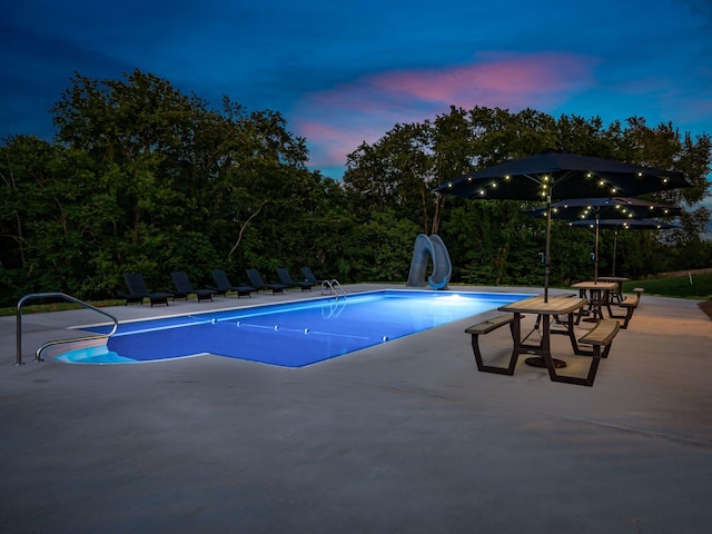 pool at dusk featuring a patio and a water slide