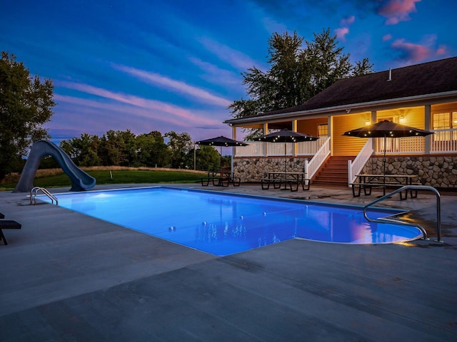 pool at dusk with a water slide, exterior bar, and a patio area