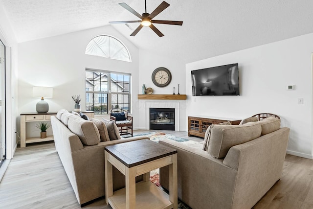 living room featuring ceiling fan, high vaulted ceiling, a textured ceiling, and light wood-type flooring