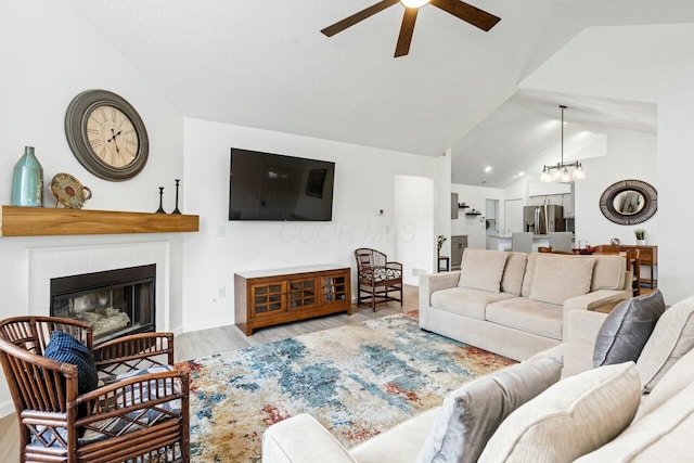 living room with high vaulted ceiling, ceiling fan with notable chandelier, a fireplace, and light hardwood / wood-style floors