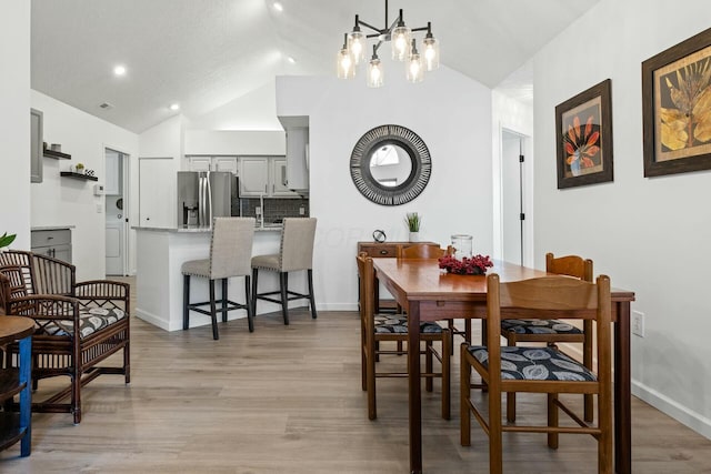 dining area with washer / dryer, lofted ceiling, a chandelier, and light wood-type flooring