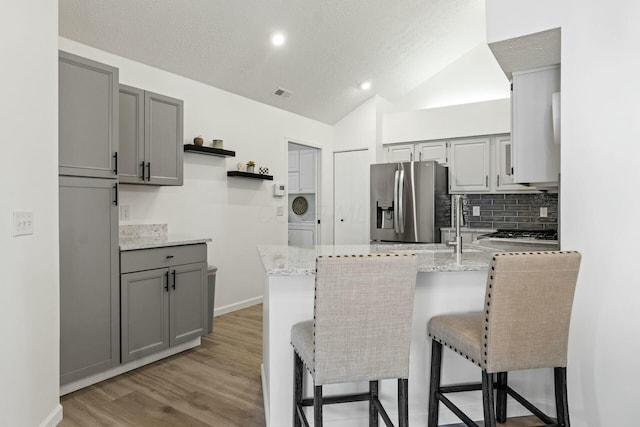 kitchen featuring stainless steel refrigerator with ice dispenser, gray cabinetry, and light stone counters