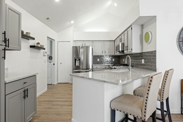 kitchen with gray cabinets, vaulted ceiling, sink, stainless steel fridge, and light stone counters