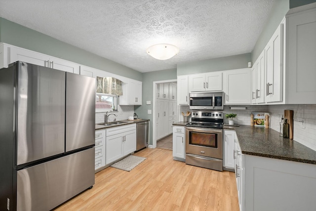 kitchen with sink, light hardwood / wood-style flooring, backsplash, stainless steel appliances, and white cabinets