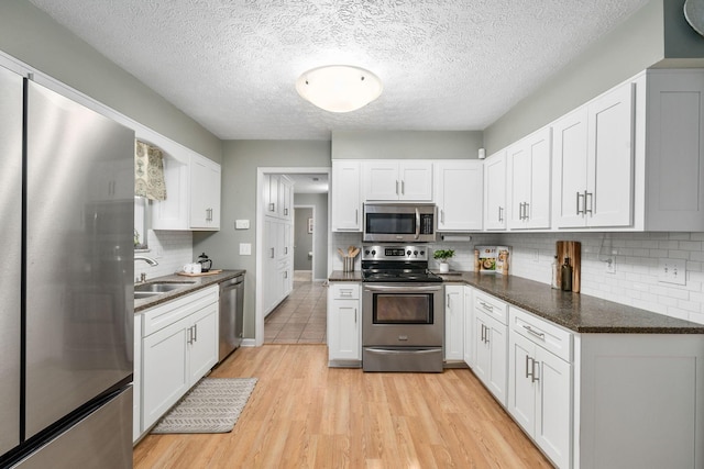 kitchen featuring appliances with stainless steel finishes, white cabinetry, sink, dark stone countertops, and light wood-type flooring