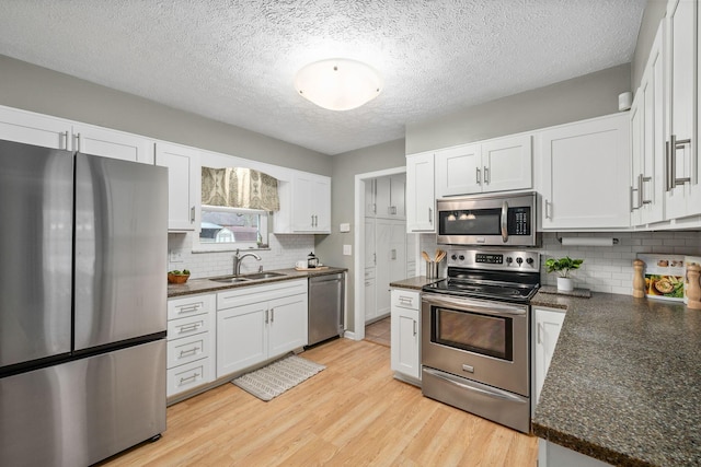 kitchen featuring sink, dark stone countertops, stainless steel appliances, light hardwood / wood-style floors, and white cabinets