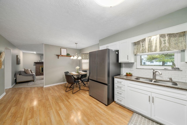 kitchen with white cabinetry, sink, pendant lighting, and stainless steel fridge