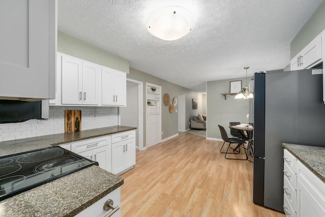 kitchen featuring pendant lighting, white cabinetry, stainless steel fridge, dark stone counters, and light hardwood / wood-style floors