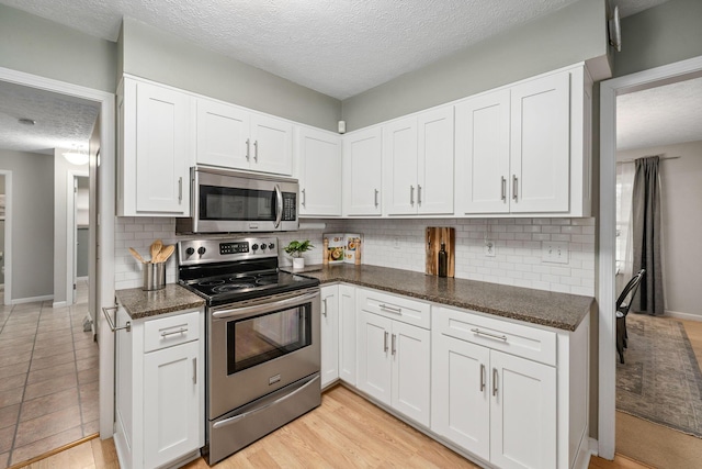 kitchen featuring white cabinetry, tasteful backsplash, dark stone counters, and appliances with stainless steel finishes