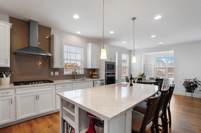 kitchen with wall chimney range hood, sink, hanging light fixtures, an island with sink, and white cabinets