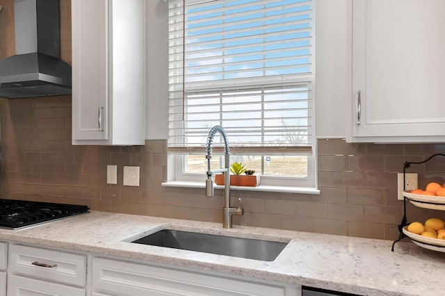 kitchen with white cabinets, light stone countertops, sink, and wall chimney exhaust hood