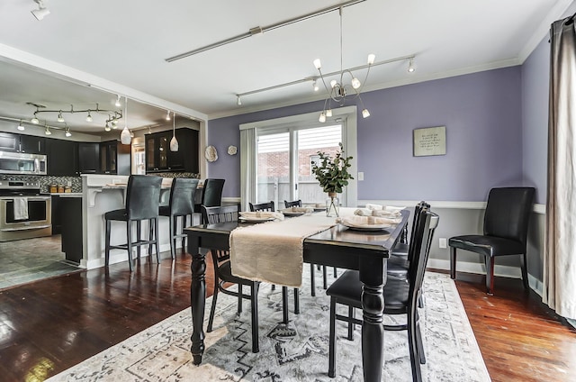 dining room featuring crown molding, dark hardwood / wood-style flooring, an inviting chandelier, and rail lighting