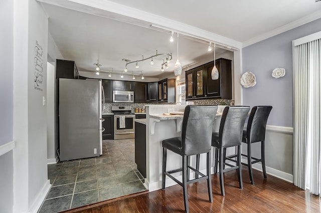 kitchen featuring appliances with stainless steel finishes, a kitchen breakfast bar, decorative backsplash, hanging light fixtures, and dark brown cabinetry