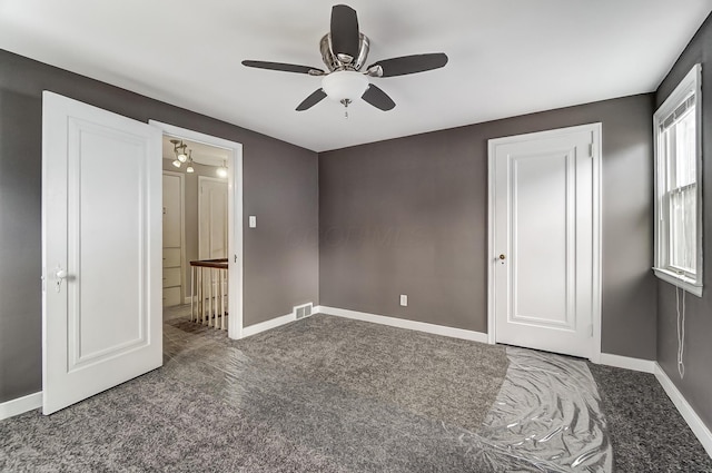 unfurnished bedroom featuring ensuite bathroom, ceiling fan, and dark carpet