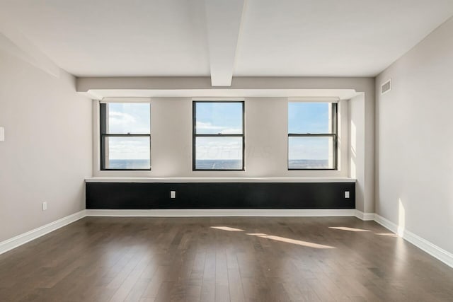 spare room with beam ceiling and dark wood-type flooring