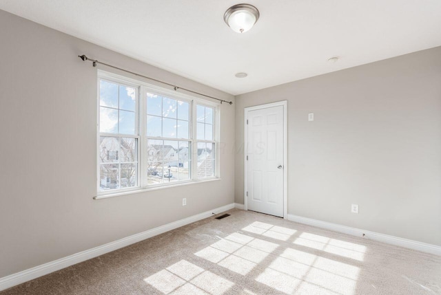 spare room featuring light colored carpet, visible vents, and baseboards