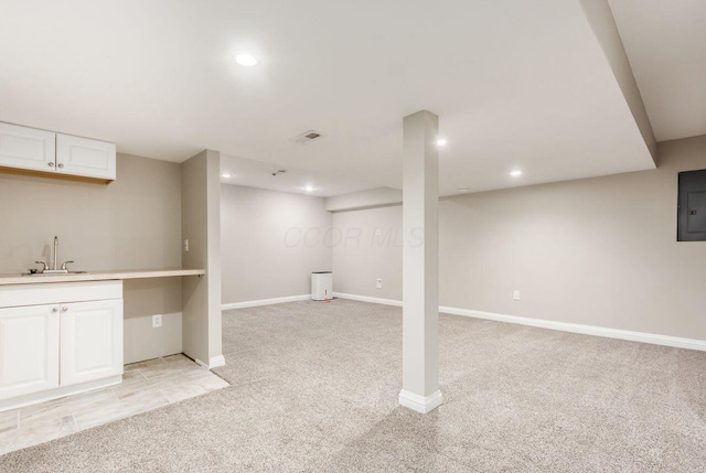 finished below grade area featuring recessed lighting, light colored carpet, a sink, baseboards, and electric panel