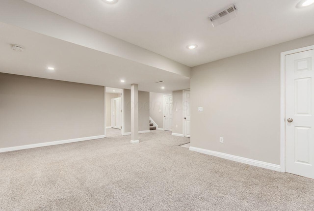 finished below grade area featuring light carpet, visible vents, stairway, and baseboards