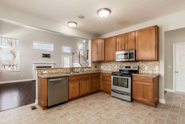 kitchen with a fireplace, stainless steel appliances, light countertops, brown cabinetry, and a sink