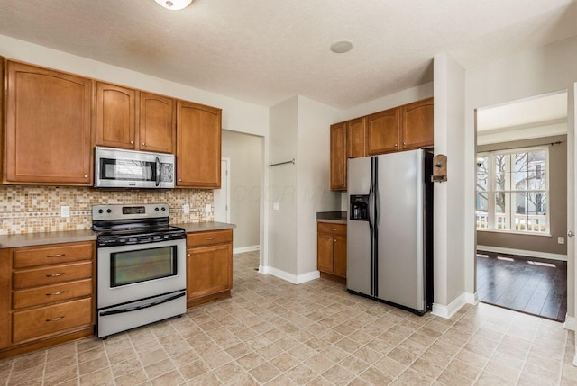 kitchen featuring baseboards, appliances with stainless steel finishes, brown cabinets, a textured ceiling, and backsplash