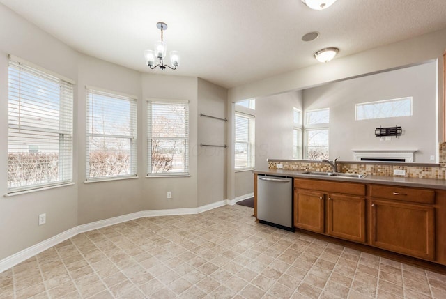 kitchen with brown cabinets, hanging light fixtures, stainless steel dishwasher, a sink, and baseboards