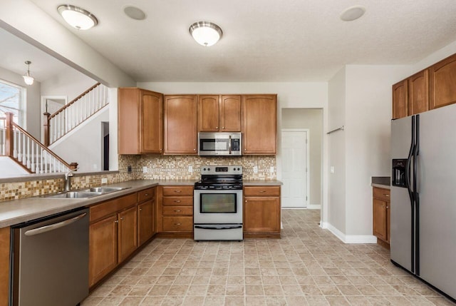 kitchen with a sink, appliances with stainless steel finishes, backsplash, brown cabinets, and pendant lighting