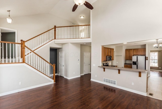 unfurnished living room featuring ceiling fan with notable chandelier, visible vents, baseboards, stairway, and dark wood finished floors