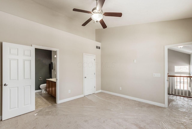 unfurnished bedroom featuring baseboards, visible vents, light colored carpet, ensuite bath, and vaulted ceiling