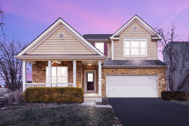 traditional-style house featuring aphalt driveway, roof with shingles, a porch, an attached garage, and stone siding