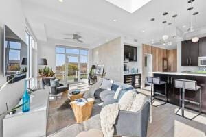 living room with ceiling fan, a skylight, and light wood-type flooring