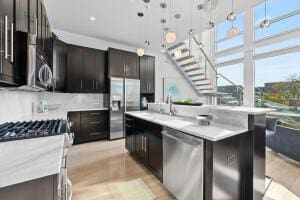 kitchen with sink, appliances with stainless steel finishes, a kitchen island with sink, hanging light fixtures, and dark brown cabinets