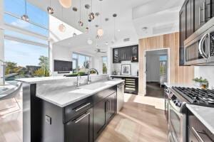 kitchen featuring appliances with stainless steel finishes, decorative light fixtures, sink, a kitchen island with sink, and light hardwood / wood-style floors