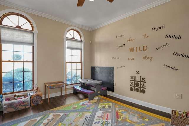 rec room with crown molding, dark wood-type flooring, ceiling fan, and a healthy amount of sunlight