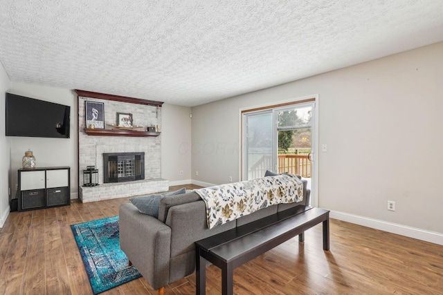 living room with wood-type flooring, a brick fireplace, and a textured ceiling