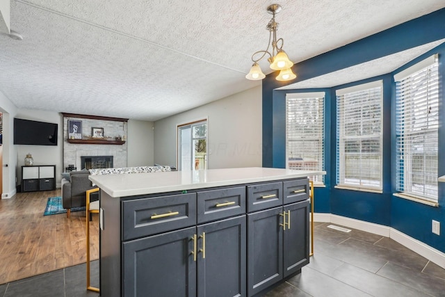 kitchen featuring a stone fireplace, gray cabinets, a center island, a textured ceiling, and decorative light fixtures