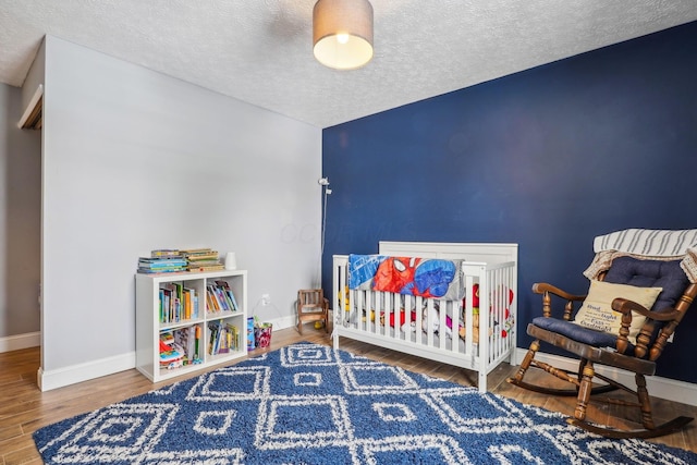 bedroom with wood-type flooring, a nursery area, and a textured ceiling