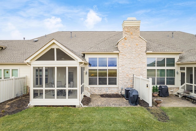 rear view of house featuring a shingled roof, a sunroom, stone siding, a lawn, and a patio area