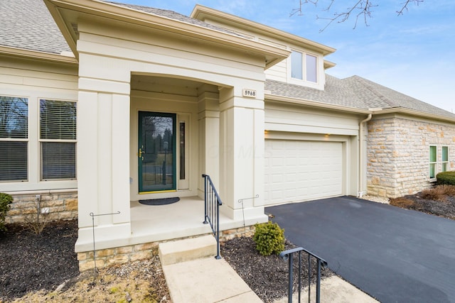 property entrance with aphalt driveway, stone siding, roof with shingles, and an attached garage