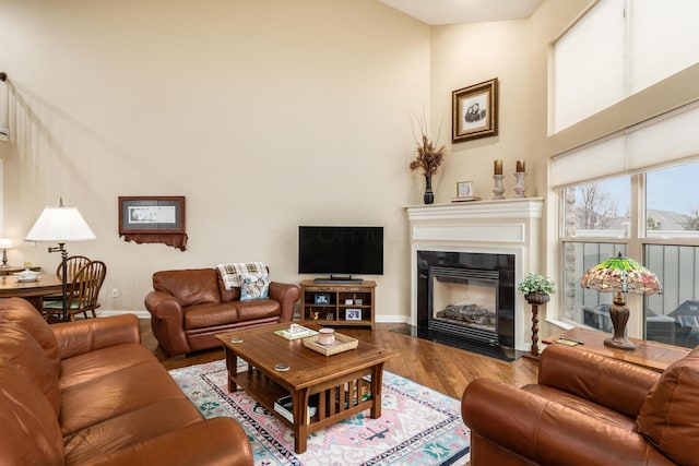 living area with a fireplace with flush hearth, a high ceiling, baseboards, and wood finished floors