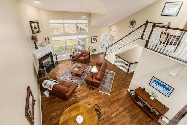 living room with a fireplace with flush hearth, ceiling fan, stairway, wood finished floors, and high vaulted ceiling