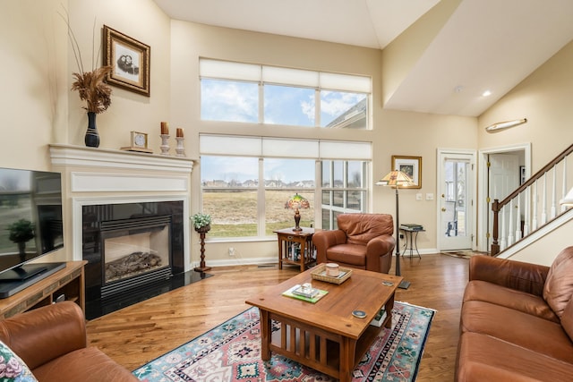 living area featuring baseboards, a fireplace with flush hearth, wood finished floors, stairs, and high vaulted ceiling