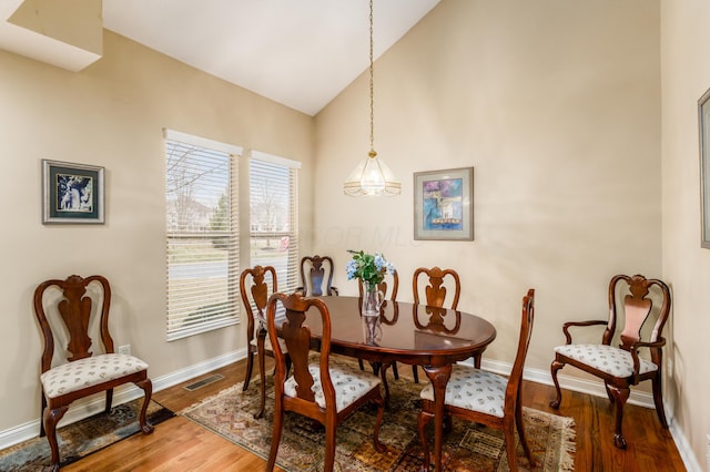 dining area with lofted ceiling, baseboards, visible vents, and wood finished floors