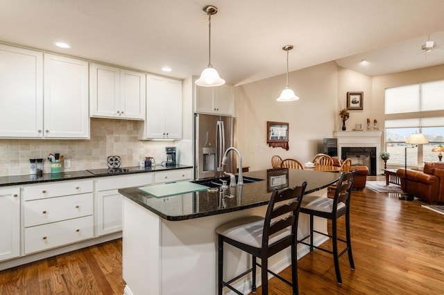 kitchen featuring wood finished floors, stainless steel refrigerator with ice dispenser, a kitchen bar, decorative backsplash, and a glass covered fireplace