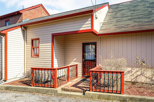 view of exterior entry with roof with shingles and brick siding