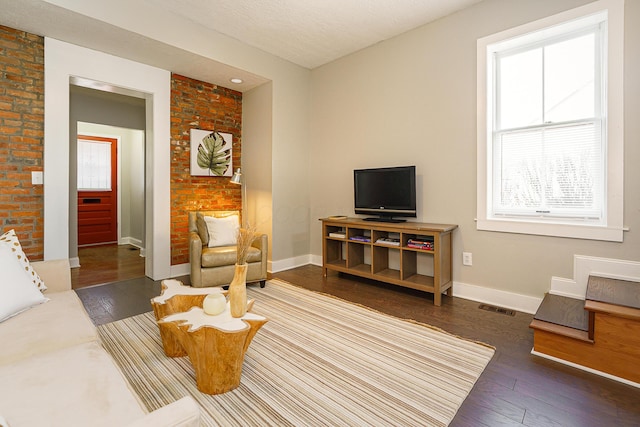 living room with brick wall, wood-type flooring, visible vents, and baseboards