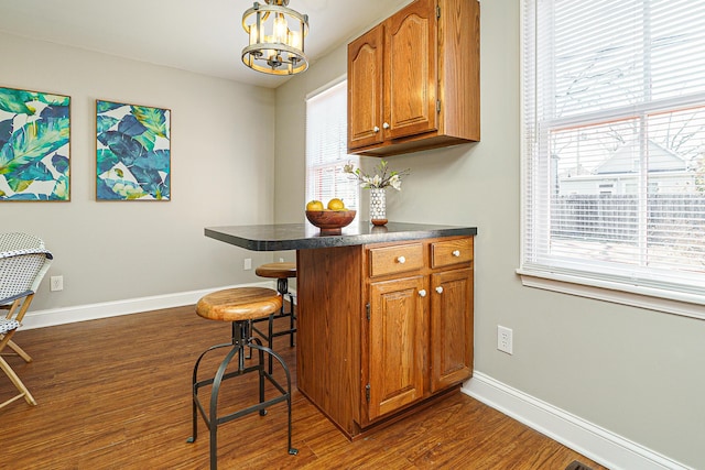 kitchen with dark wood-style floors, brown cabinets, dark countertops, a kitchen breakfast bar, and baseboards