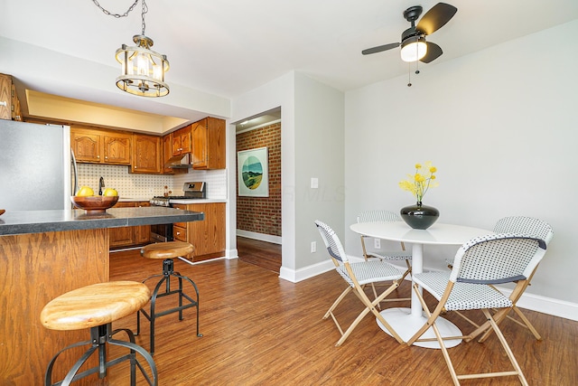 kitchen with brown cabinets, stainless steel appliances, decorative backsplash, wood finished floors, and under cabinet range hood