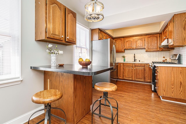 kitchen with appliances with stainless steel finishes, brown cabinets, a peninsula, and a breakfast bar area