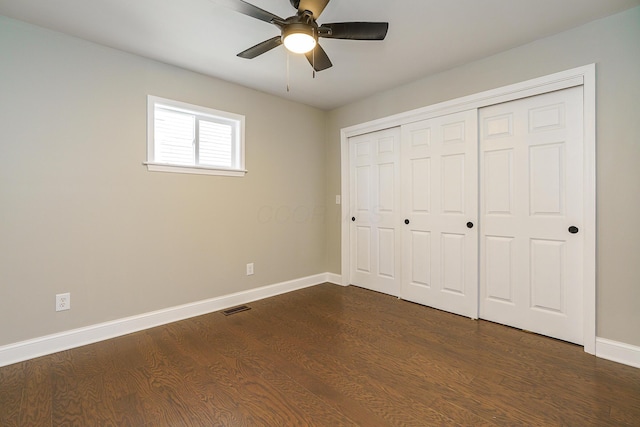 unfurnished bedroom featuring dark wood-style flooring, a closet, visible vents, and baseboards